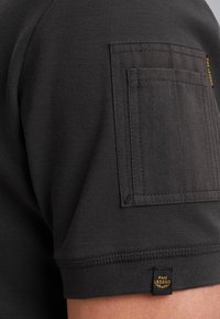 Zwarte kortemouwen shirt met een textuurweefsel, een patch zak op de mouw en een merklabel aan de zoom.