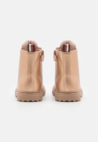 Stivali alla caviglia color nocciola con finitura in pelle liscia, cerniere posteriori e suole in gomma texture. Presentano un accento a strisce sul tallone.