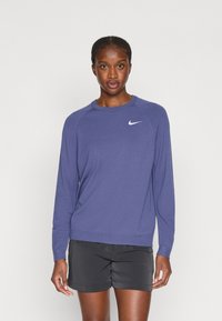 Violeta garā piedurkne sporta krekls, kas izgatavots no mīksta materiāla, ar apaļu kakla izgriezumu, ribotām aprocēm un mazu baltu Nike logo uz krūtīm.