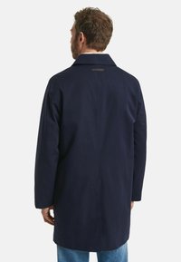 Marineblauwe jas met een kraag, lange mouwen en een rugsplit. Glad stof met een label detail op de kraag. Lichtgewicht en recht gesneden.
