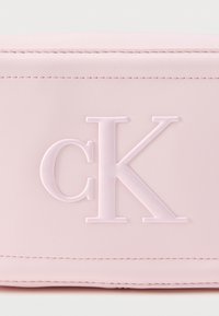 Λογότυπο CK με ανάγλυφη επιφάνεια σε απαλό ροζ δέρμα με ορατή ραφή κατά μήκος των άκρων, κοντινή λήψη.