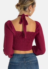 Bordeaux cropped top med puffede ærmer og smocked rygdetalje. Bindes omkring halsen og den glatte stoftekstur supplerer designet.