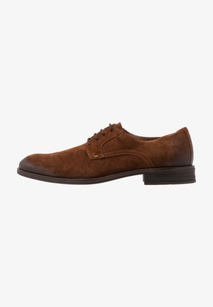 Scarpa da uomo in suede marrone, con punta rotonda, lacci in pelle e tacco piatto. Dettaglio di cucitura laterale sulla parte superiore e suola liscia.