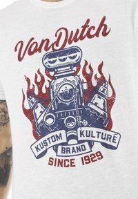 T-shirt blanc en coton avec un imprimé graphique d'un moteur vintage avec des flammes rouges, accompagné du texte bleu "Von Dutch Kustom Kulture Brand Since 1929."
