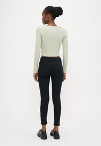 Mintno zelena rebrasta majica z dolgimi rokavi v kombinaciji s črnimi ozkimi jeans hlačami. Model nosi črne čevlje. Čist dizajn s prilegajočo se silhueto.