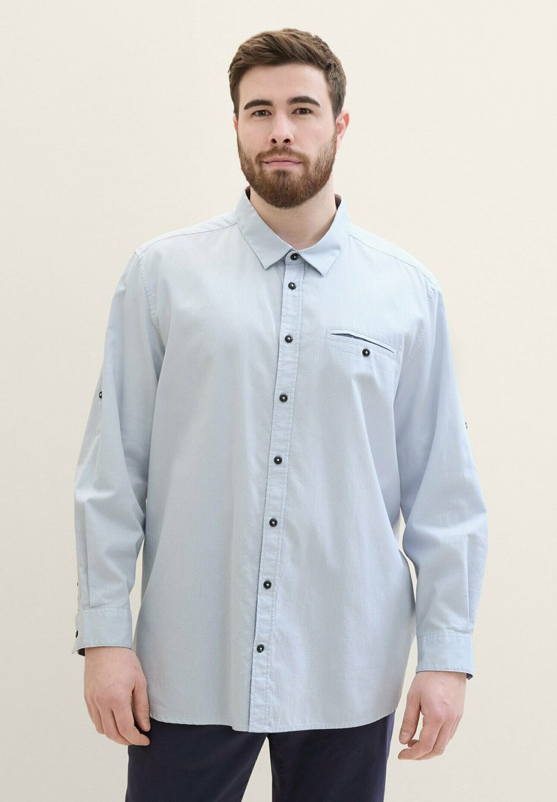 Hellblaues Button-Up-Hemd mit strukturiertem Muster, schwarzen Knöpfen und einer Brusttasche. Verfügt über lange Ärmel mit geknöpften Manschetten.