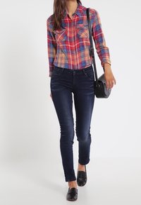 Rutig skjorta med knäppning i röd, blå och orange, matchad med mörka tighta jeans; svarta låga skor; liten svart axelväska.