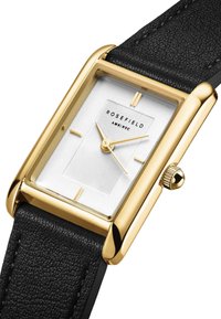 Orologio rettangolare dorato con quadrante bianco testurizzato, cinturino in pelle nera e accenti dorati minimalisti. Presenta una corona per le regolazioni.