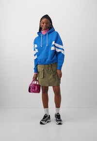 Blå huvtröja med vita ränder, olivgrön cargokjol, rosa handväska, vita strumpor och svarta sneakers. Slät tygkvalitet med avslappnad passform.