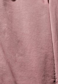 Gerimpelde, zacht gematerialiseerde stof in een gedempte, stoffige rozenkleur met subtiele plooien en schaduwen over het oppervlak.