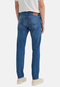 Jeans de mezclilla azul con corte recto, que cuentan con dos bolsillos traseros y una etiqueta de cuero. Diseño simple sin patrones o adornos visibles.