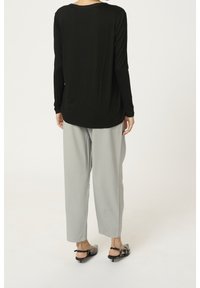 Person set bagfra iført en sort bluse med lange ærmer, lysegrå bukser med vide ben og sorte slingback-sko med lav hæl.