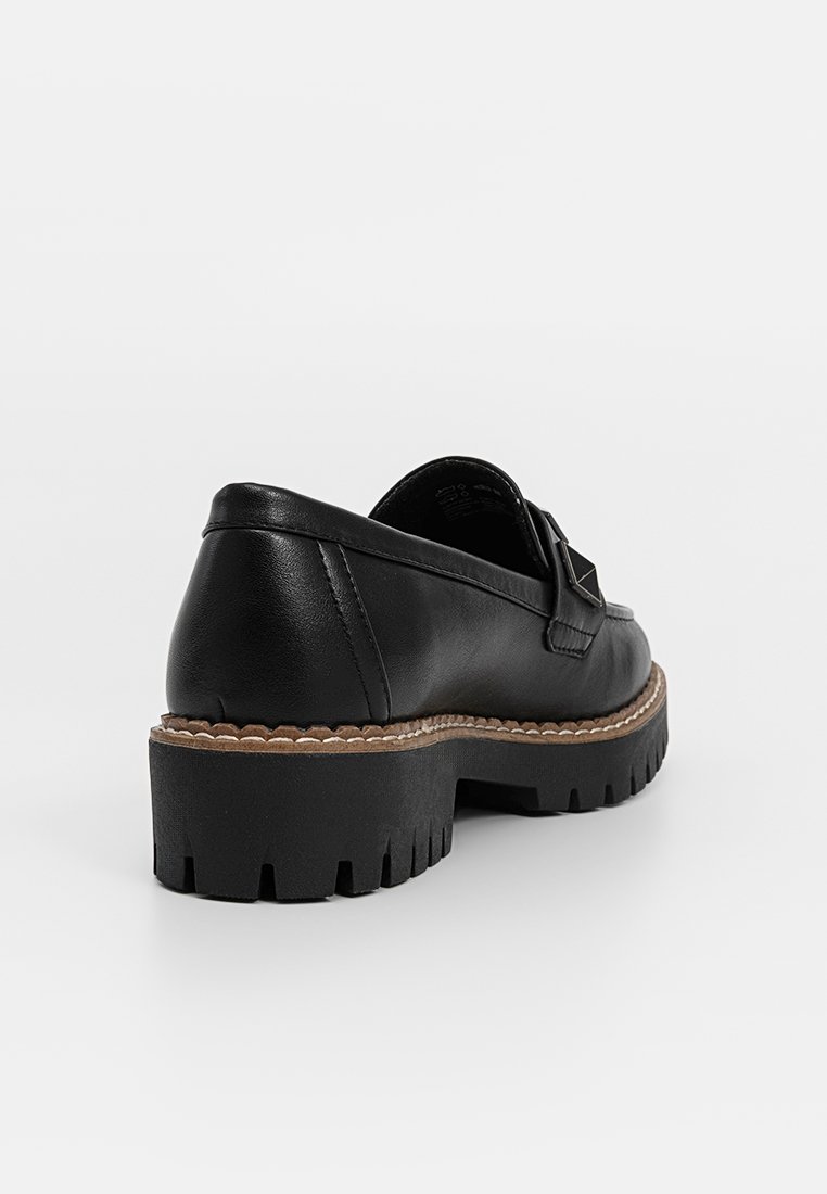 Scarpa nera in pelle scamosciata con suola spessa e dalla texture marcata, caratterizzata da una distintiva fasciatura decorativa e da cuciture a contrasto lungo il bordo.