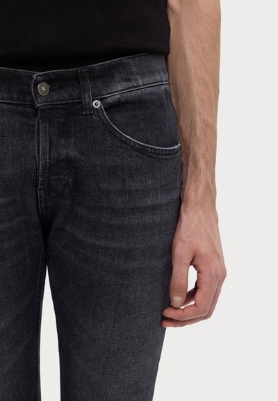 Jeans in denim scuro con una texture liscia, taglio slim e cuciture visibili. Presentano una tasca frontale e una chiusura con bottone in metallo.