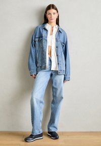 Giacca di jeans azzurro chiaro con una vestibilità comoda, abbinata a jeans azzurri chiari e una camicia bianca con bottoni. Sneakers nere con suola bianca.