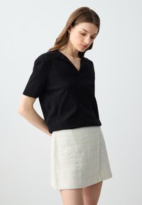 Polo shirt noir à manches courtes avec une texture douce et lisse, associé à une mini-jupe en tweed blanc au fini texturé.