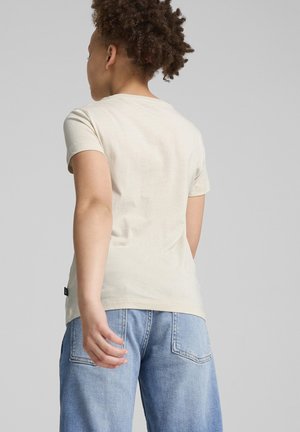 T-shirt beige clair à manches courtes avec un col rond, fabriqué en coton doux, associé à un jean bleu clair à coupe ample avec des poches arrière.