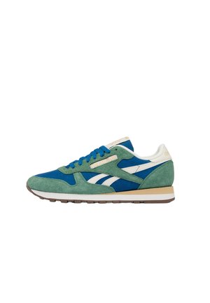 Low-cut sneaker with blue fabric, green suede overlays, white side stripes, blue laces, and beige sole with white and brown layers.