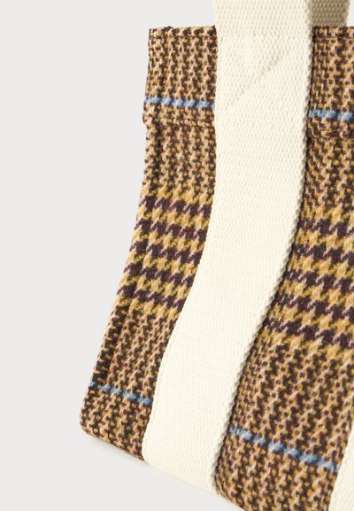 Sac fourre-tout en tissu à carreaux marron, jaune et noir, avec de larges anses tissées en blanc cassé sur un fond blanc.