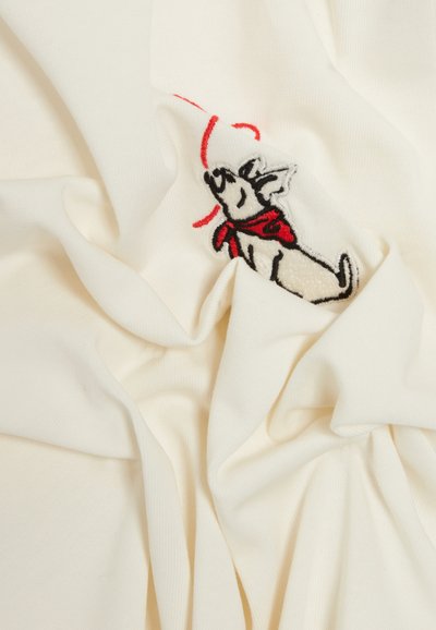 Tissu blanc avec une surface texturée, comportant des détails brodés d'un chien portant une écharpe rouge. Le design inclut des coutures ludiques en noir et rouge.