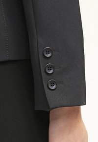 Manche de veste de costume noire avec trois boutons noirs, texture lisse, coupe ajustée et détail de couture subtil.