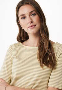 Pruhované tričko v světle béžové a krémové barvě, s krátkými rukávy a širokým výstřihem. Měkká tkanina s mírně přiléhavým střihem a detailem loga.