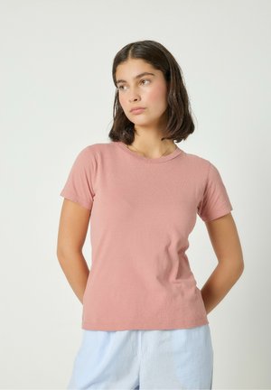T-shirt a maniche corte con scollo rotondo in morbido cotone rosa cipria, dalla linea aderente e con una texture leggera. Abbinata a pantaloni a righe azzurro chiaro.