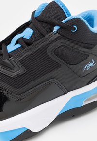 Černé tenisky s texturovaným svrškem a lesklými akcenty, s modrými detaily na jazyku a mezipodešvi a bílou podrážkou.