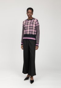 Maglione lavorato a maglia in un motivo a quadri rosa e nero con una texture pelosa, abbinato a pantaloni neri larghi e mule neri a punta.