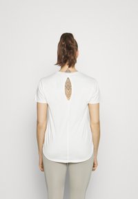 Witte t-shirt met korte mouwen en een sleutelgatcut-out aan de achterkant, van zachte stof en met een relaxte pasvorm. Draag het met lichtgekleurde leggings.