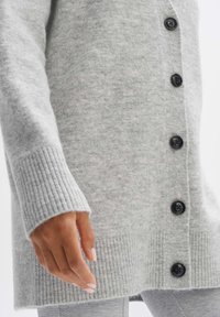 Šedý vlněný kardigan s žebrovaným lemem na manžetách a spodním okraji, šesti černými knoflíky vpředu a měkkým, strukturovaným povrchem.
