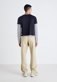 Haut à manches courtes bleu marine sur des manches longues rayées, associé à un pantalon beige et des chaussures beiges. Présente une coupe décontractée et confortable.