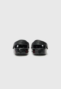 Black Crocs with a shiny finish, featuring adjustable straps, red dot accents, and a circular ventilation port on the sides.