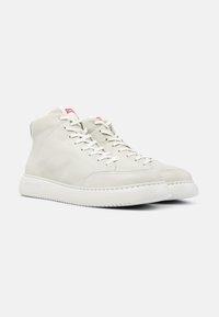 Zapatillas altas blancas de cuero suave, con cierre de cordones, cuello acolchado y suela de goma texturizada. Acento del logo rojo en la lengua.