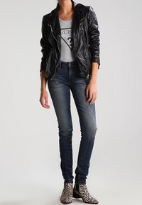 Chaqueta de moto de cuero negra, camiseta gris, jeans skinny de mezclilla oscura y botas de tobillo con estampado de leopardo. Texturas suaves y patrones variados.