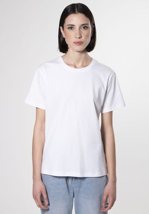 Maglietta bianca in cotone con collo rotondo, maniche corte e vestibilità rilassata, abbinata a jeans in denim azzurro chiaro.