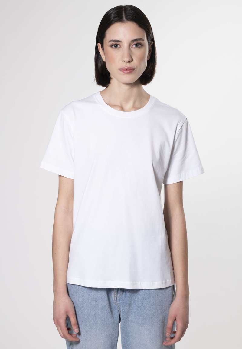 Camiseta blanca de algodón con cuello redondo, mangas cortas y un corte relajado, combinada con jeans de denim azul claro.