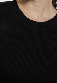 Pull en maille côtelée noire avec un col rond et un tissu texturé, présentant de fines lignes horizontales et une couture uniforme autour du col.