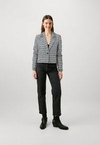 Krótka, teksturowana marynarka w czarno-białym kolorze z klapami, podwójnymi guzikami i kontrastową lamówką. Połączona z czarnymi dżinsami i botkami za kostkę.