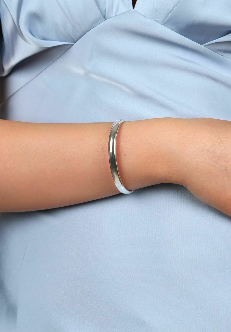 Silver armband på en ljusblå ärm, med en slät, rundad design och en polerad yta.