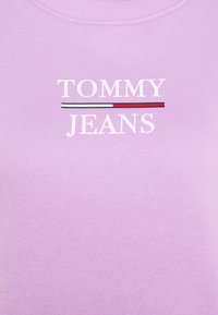 Lila bomullströja med texten "TOMMY JEANS" i vitt, med en horisontell randaccent i rött, vitt och blått.