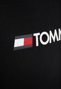 Black textile featuring a prominent white logo reading "TOMMY." Logo includes a rectangular design with red, white, and blue accents positioned to the left.