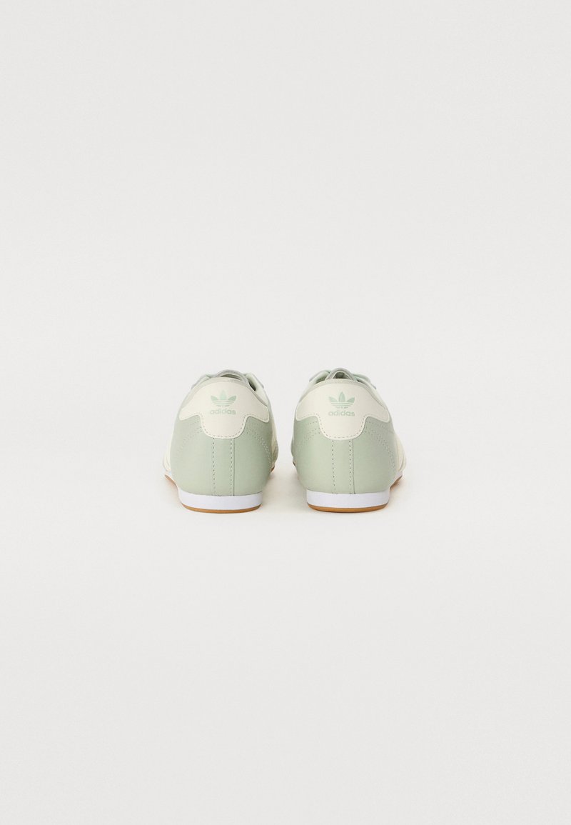 Zapatillas verdes y crema con un acabado de cuero suave, forma redondeada, suela de goma blanca y detalles de marca en el talón y la lengüeta.