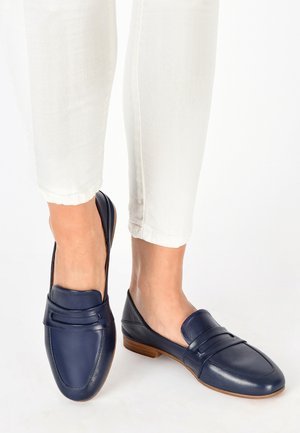 Mørkeblå læder loafers med lav hæl, der har en tekstureret strop over forsiden og åben hæl, parret med hvide cropped bukser.