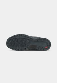 Black athletic shoe sole with textured rubber for grip, featuring different tread patterns and a small red accent on the heel.