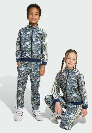 Des survêtements floraux avec des accents bleu marine, une veste zippée et un pantalon assorti. Comprend des rayures blanches sur les manches et les côtés, avec des chaussures contrastantes.