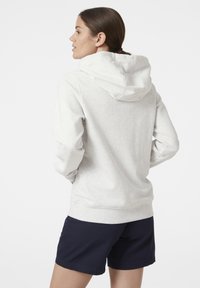 Sudadera gris claro con capucha ajustable, textura suave, puños y dobladillo acanalados. Combinada con pantalones cortos azul marino. Vista trasera mostrada.