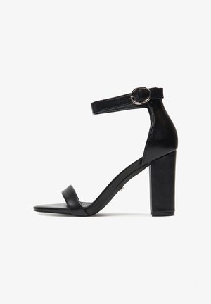 Sandalia negra de tacón ancho, con tiras finas en el tobillo y textura de cuero suave. Diseño sencillo y minimalista con punta abierta.