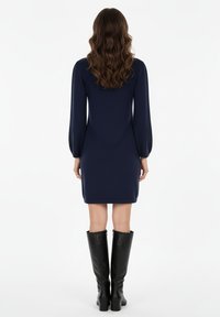Abito blu navy, lungo fino al ginocchio, con maniche lunghe, tessuto liscio e silhouette aderente, abbinato a stivali neri in pelle al ginocchio.