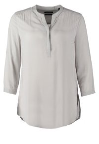 Blouse gris clair à manches longues avec un col bande et une patte de boutonnage partielle à l’avant, avec des fronces subtiles aux épaules et des fentes latérales.